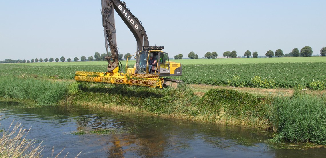 A Herder mowing bucket cutting back vegetation along a water course