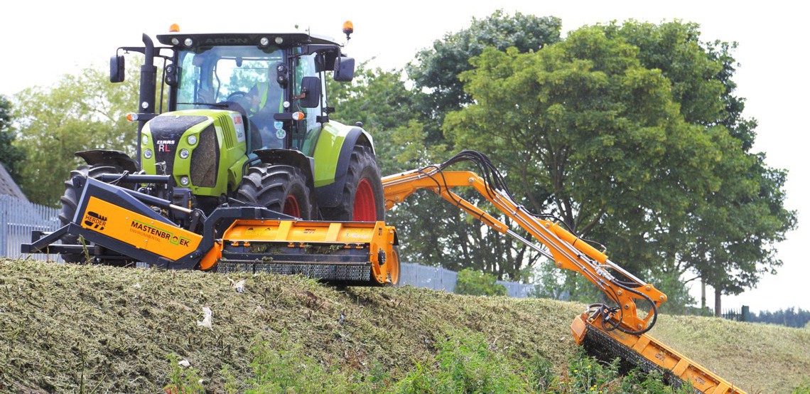 A Herder tractor-mounted long reach arm trimming vegetation growth alongside a water course